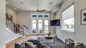 Un vaste espace de vie comprenant un escalier, un ventilateur de plafond, un téléviseur à écran plat et une grande fenêtre donnant sur l’extérieur.