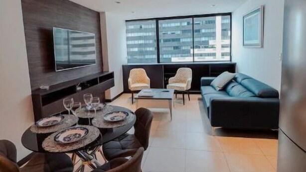 A modern living room with a dining area, a sofa, and a TV mounted on the wall. - Puerto Santa Ana , automatic check in, Parking (Guayaquil)