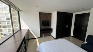 A modern bedroom with a large bed, a TV mounted on a wooden panel, a wardrobe, and a balcony with a city view. - Puerto Santa Ana , automatic check in, Parking (Guayaquil)
