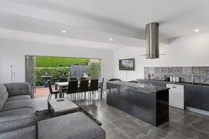 A modern kitchen with a central island, a dining area with a sofa and chairs, and a view of greenery outside. - Ellis Cottage Glebe Luxury 1 - 4 bedroom Cottage, Hobart, Tasmania (Glebe)