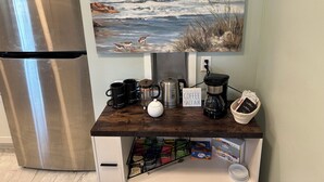Eine Küche mit einem Edelstahl-Kühlschrank, einer Kaffeestation mit Tassen und einer Kaffeemaschine, sowie einem Gemälde mit Strandmotiv.