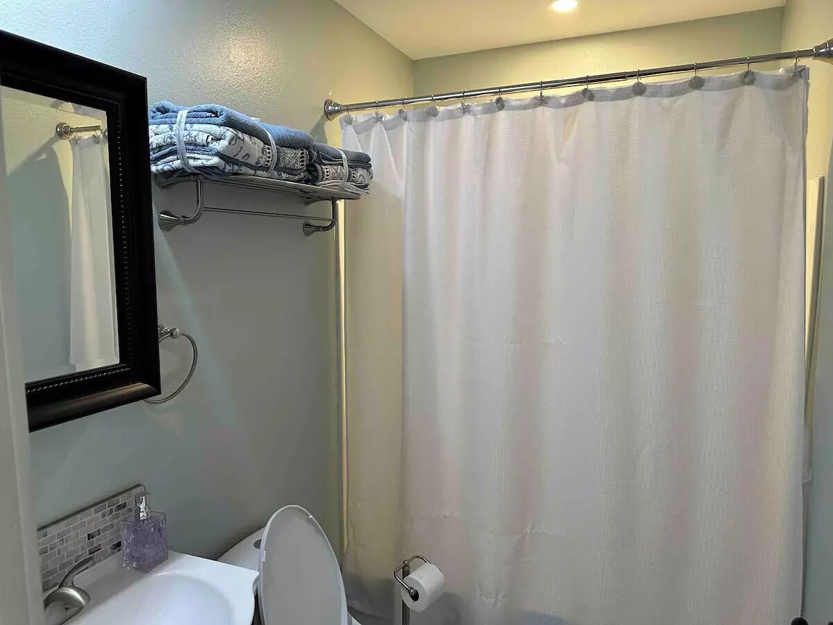 A bathroom with a white sink, a mirror, a towel rack with folded towels, and a shower curtain.