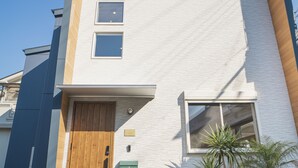 A modern two-story house with a wooden front door, a small window, and a green mailbox. - Orange County Guest House - Hostel  (Izumisano)