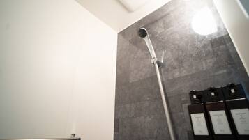 A shower area with a handheld showerhead, a towel rack, and a wall-mounted control panel.