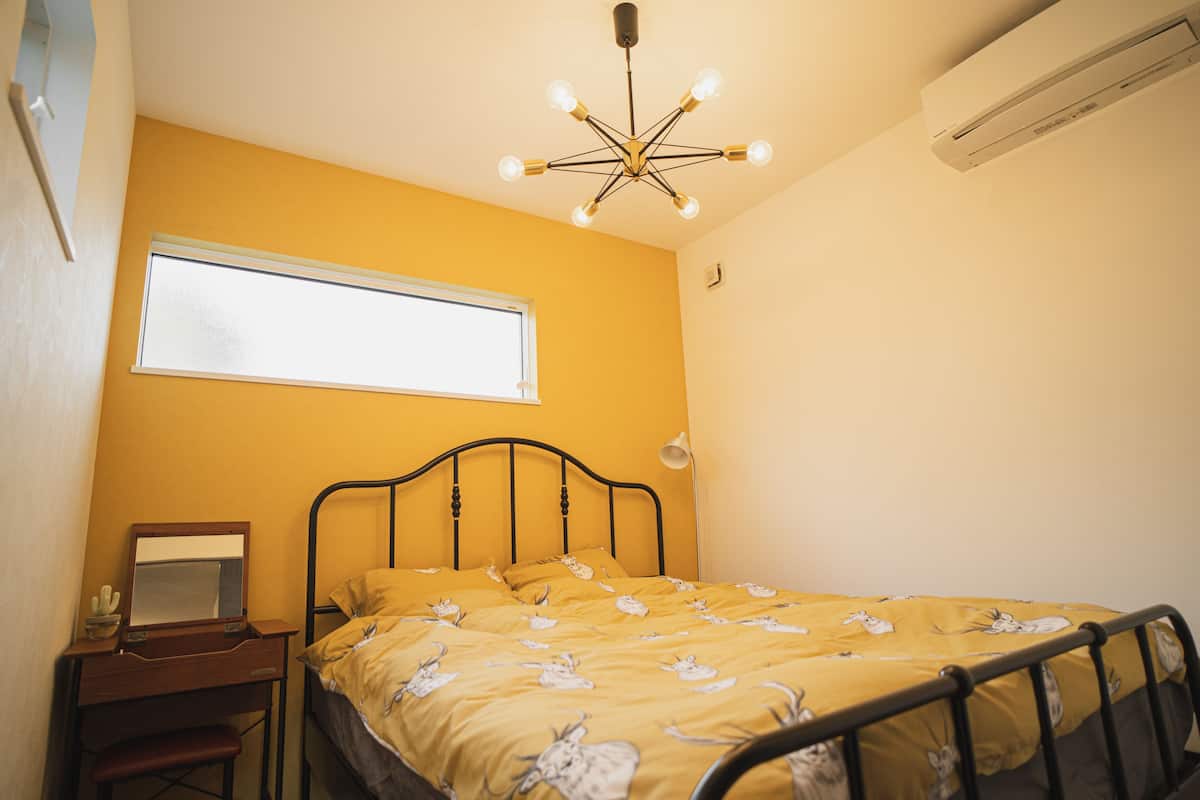 A bedroom with a bed, a desk, a chair, a window, and a ceiling light fixture.