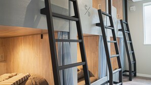 Bunk beds with wooden headboards, a ladder, and a window with curtains. - Orange County Guest House - Hostel  (Izumisano)