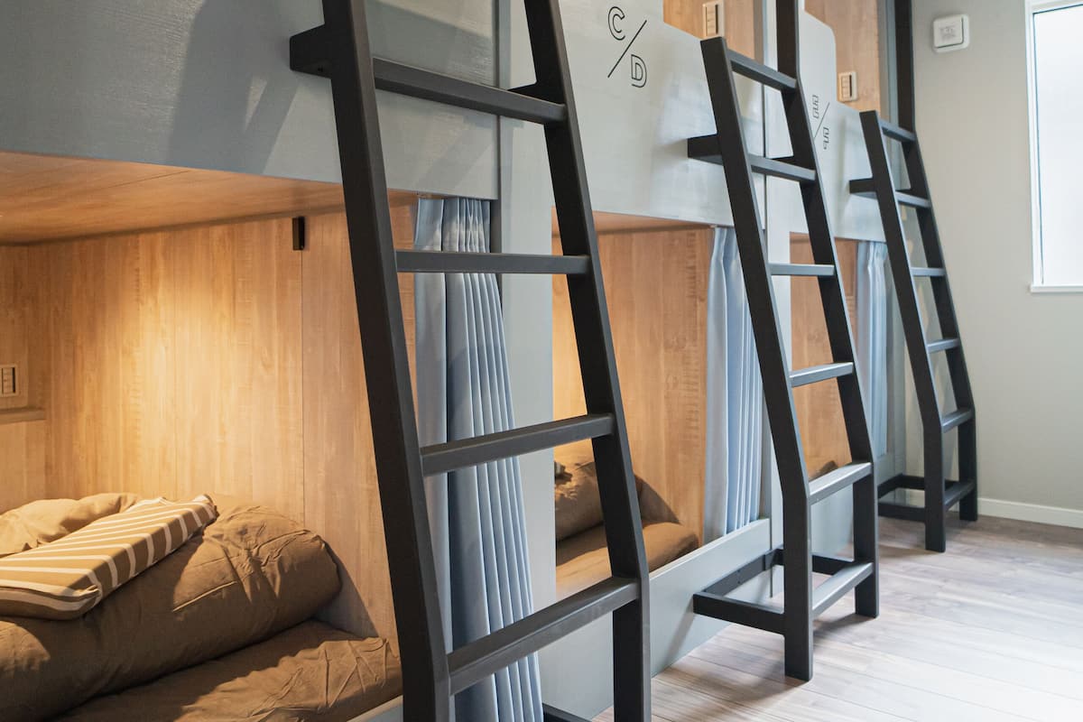 Bunk beds with wooden headboards, a ladder, and a window with curtains.