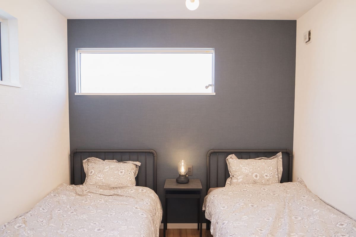 A room with two beds, a ceiling light fixture, a nightstand, and a window.