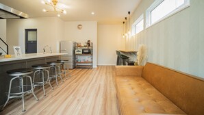 A modern kitchen with a bar area, a sofa, and a dining table. - Orange County Guest House - Hostel  (Izumisano)