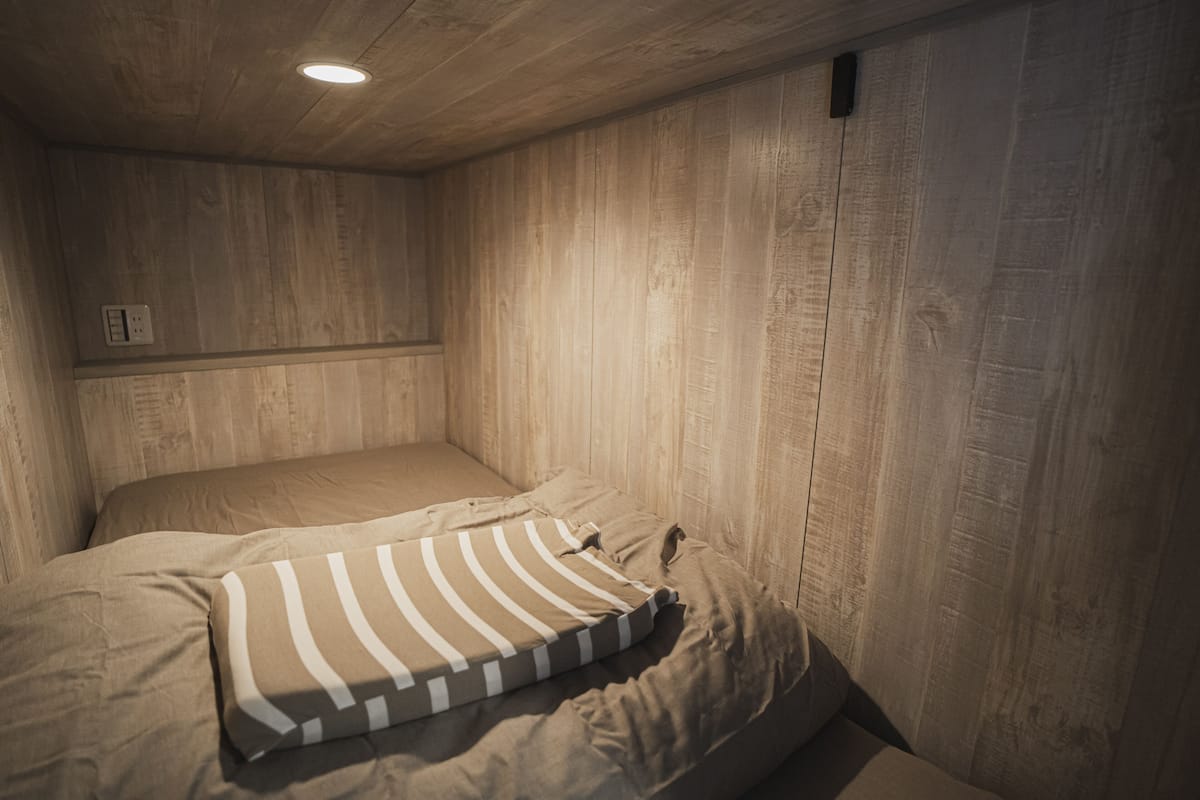 A single bed with a striped pillow in a room with wooden panel walls and a ceiling light.