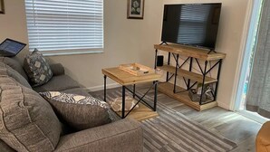 A living room with a sofa, a coffee table, a TV on a stand, and a bookshelf. - Beachside 1/1 apartment just steps from beautiful Saint Augustine Beach (St. Augustine)