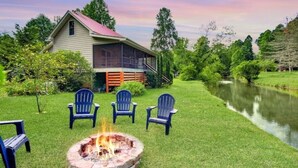 A house with a screened porch, a fire pit, and a pond in the background. - Riverside Oasis! Close to Helen and Wineries (Suches)