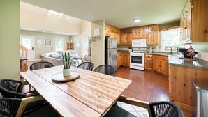 A spacious kitchen with wooden cabinets, a dining area with a wooden table, and a view of the living room. - Riverside Oasis! Close to Helen and Wineries (Suches)