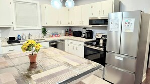 Una cocina moderna con armarios blancos, electrodomésticos de acero inoxidable y una isla central con una planta en maceta.