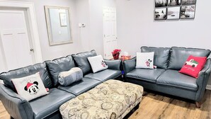 Una sala de estar moderna con un sofá de cuero gris, un reposapiés estampado y una galería de cuadros en la pared.