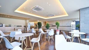Un moderno vestíbulo de hotel con una zona de estar central, una cocina al fondo y un mostrador de recepción.