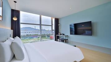 Une chambre d’hôtel moderne dotée d’un grand lit, d’un téléviseur à écran plat et offrant une vue sur un paysage lointain grâce à de grandes fenêtres.