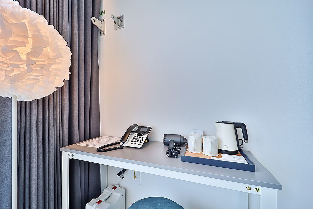 A hotel room desk with a telephone, coffee maker, and mugs.