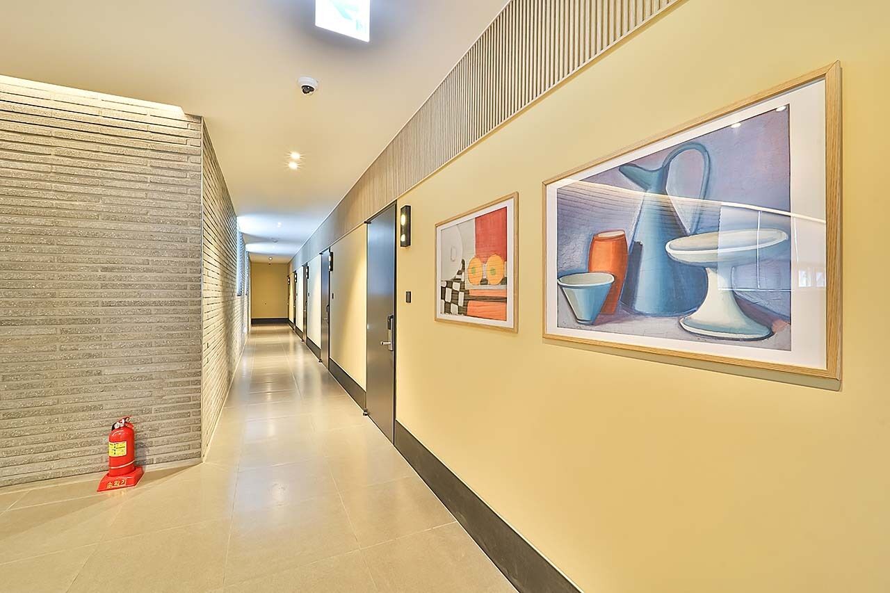 Een hotelgang met een brandblusser, een beveiligingscamera aan de muur en kunstwerken in lijsten.