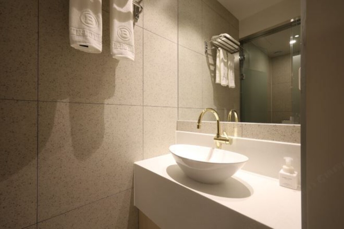 A modern bathroom with a white sink, gold faucet, and a large mirror.