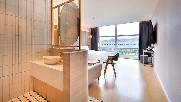 Un hotel moderno con una cama grande, una zona de estar, un baño con un espejo amplio y vistas a la ciudad.