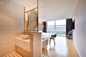 A modern hotel room with a large bed, a sitting area, a bathroom with a large mirror, and a view of the cityscape. - Browndot Busan Newport Signature (Changwon)