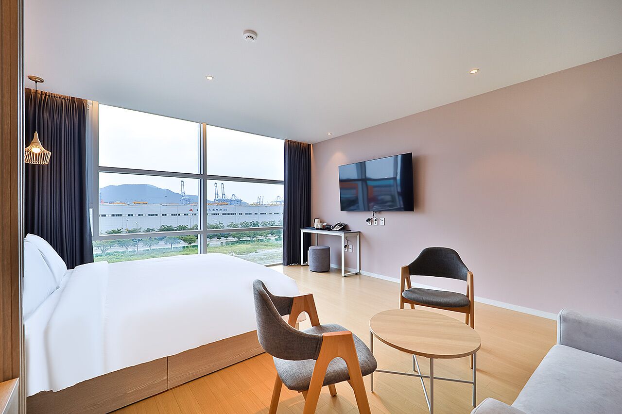 Habitación de hotel con una cama grande, un escritorio con silla, un televisor montado en la pared y vistas al aeropuerto.
