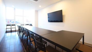 A conference room with a long table, chairs, a flat-screen TV, and large windows.