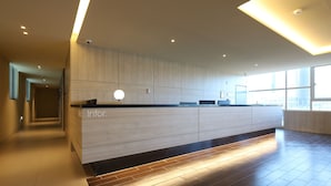 Un área de recepción moderna con un mostrador de madera, un televisor de pantalla plana y un amplio ventanal con vistas a la ciudad.