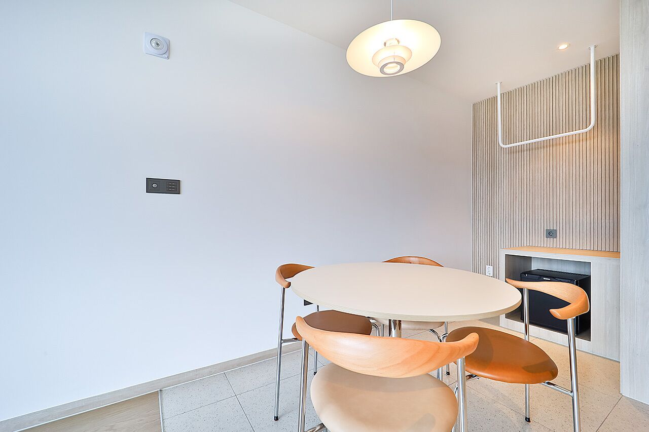 A modern dining area with a round table and four chairs, a pendant light, and a wooden panel wall.