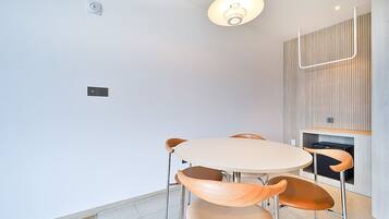 A modern dining area with a round table and four chairs, a pendant light, and a wooden panel wall.