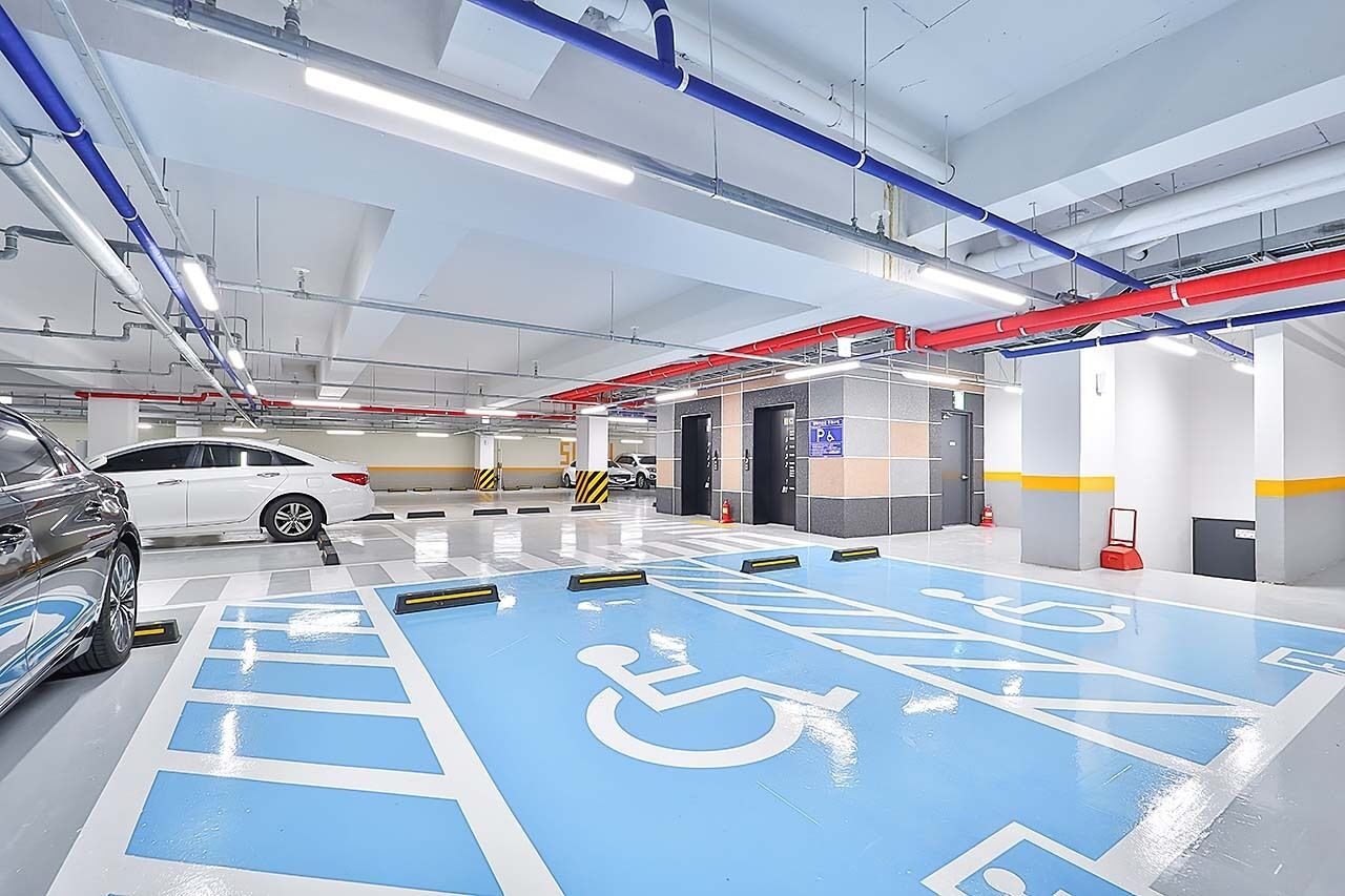 A modern indoor parking garage with blue handicapped parking spaces, white cars, and visible structural elements like pipes and lighting.