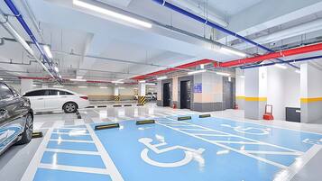 A modern indoor parking garage with blue handicapped parking spaces, white cars, and visible structural elements like pipes and lighting.
