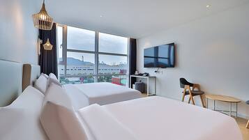 Une chambre d’hôtel avec deux lits, un bureau, une chaise, une télévision et une grande fenêtre donnant sur la ville.