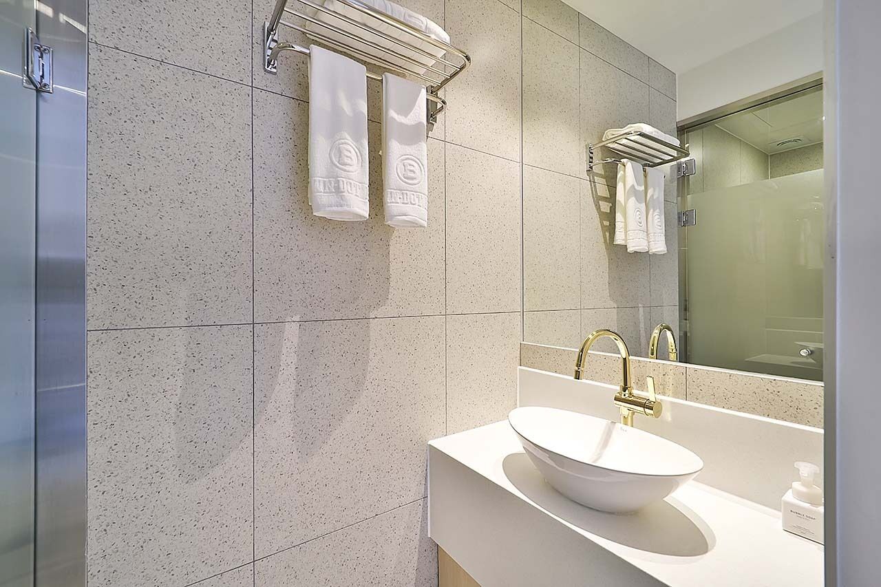Un baño moderno con lavamanos blanco, grifos dorados y cabina de ducha con mampara de vidrio.