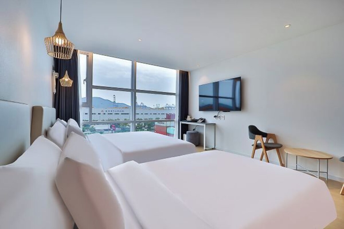 A modern hotel room with two beds, a desk, a chair, and a TV.