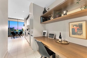 Une cuisine moderne avec un plan de travail en bois, un coin repas avec des chaises et une vue sur la ville grâce à de grandes fenêtres.