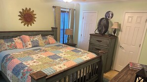 Een slaapkamer met een houten bed, een quilt, een kaptafel, een ventilator en een deur.