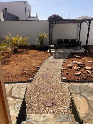 Un patio con un sendero de grava, bancos para sentarse y una estructura de pérgola.