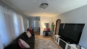 Una sala de estar con un sofá negro, un tapete estampado, un televisor y un mueble aparador.