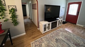 Una sala de estar con un televisor de pantalla plana sobre un mueble blanco, una alfombra estampada y una puerta roja.