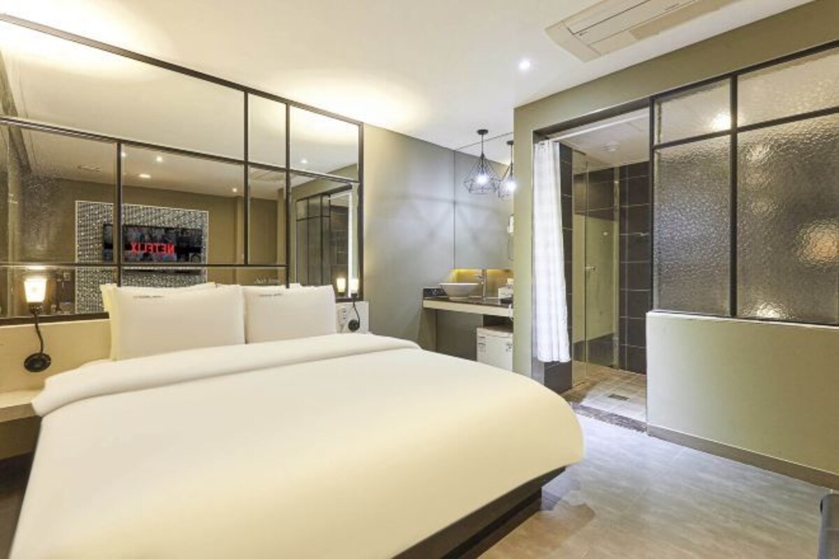 A modern bedroom with a large bed, a mirror, a vanity, and a walk-in closet.