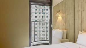 A hotel room with a large bed, a wooden headboard, and a view of a cityscape through a window. - HERTZ Hotel (Seoul)