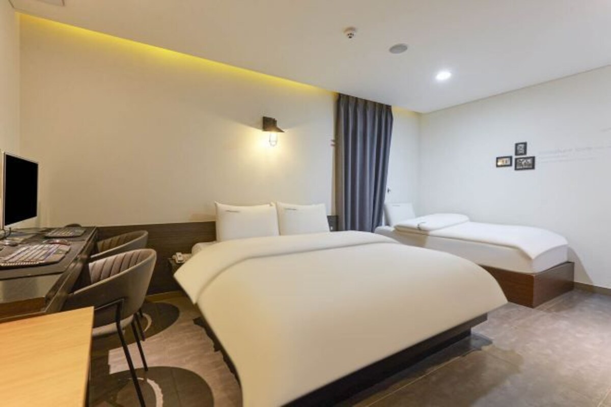 A modern hotel room with a large bed, a desk with a computer, and a chair.