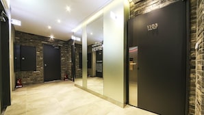 A modern hotel lobby with a stone wall, a mirrored wall, and a floor with light-colored tiles. There are doors labeled "1103" and "Tourist Hotel Hertz". - HERTZ Hotel (Seoul)
