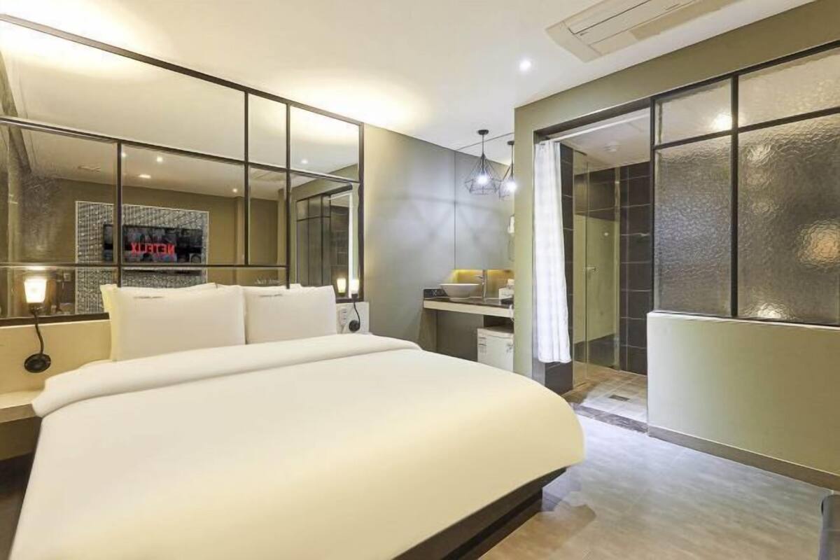 A modern bedroom with a large bed, a mirror, a vanity, and a walk-in closet.