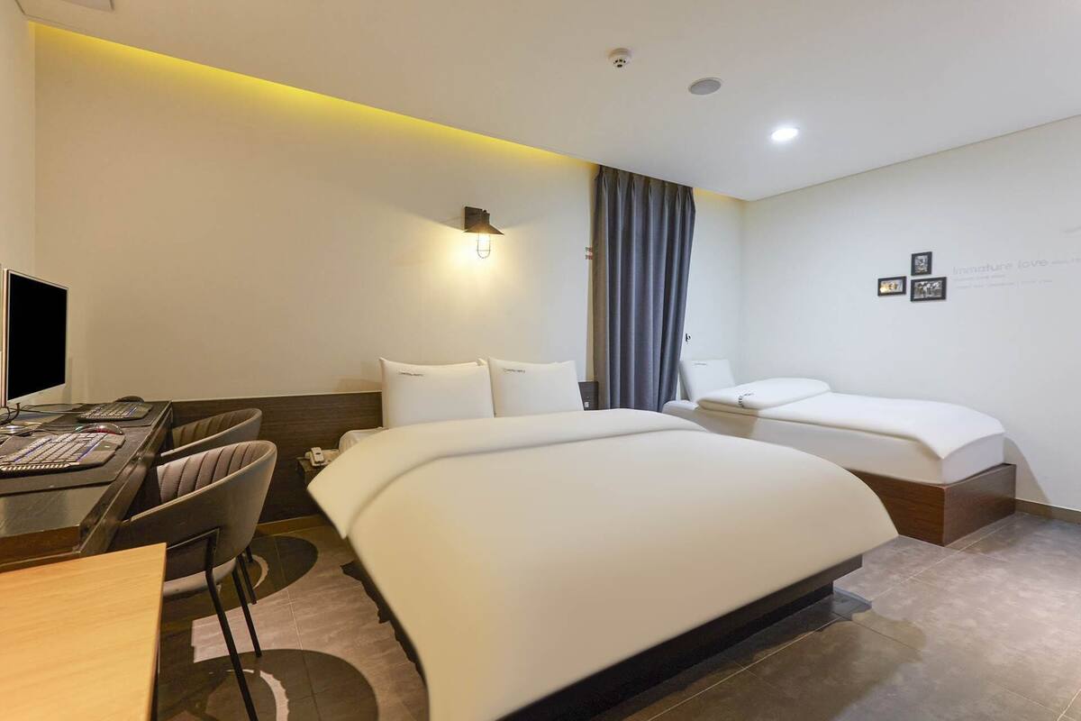 A hotel room with a bed, a desk with a computer, a chair, and a small table.