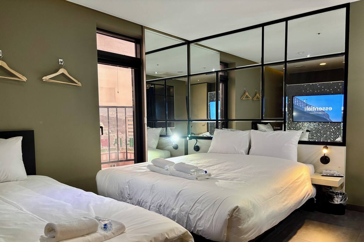 A hotel room with two beds, a TV, a balcony, and a view of the city.