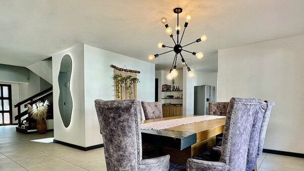 A dining area with a wooden table, six upholstered chairs, and a modern chandelier.
