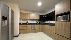 A modern kitchen with wooden cabinets, a stainless steel refrigerator, a microwave, and a sink.